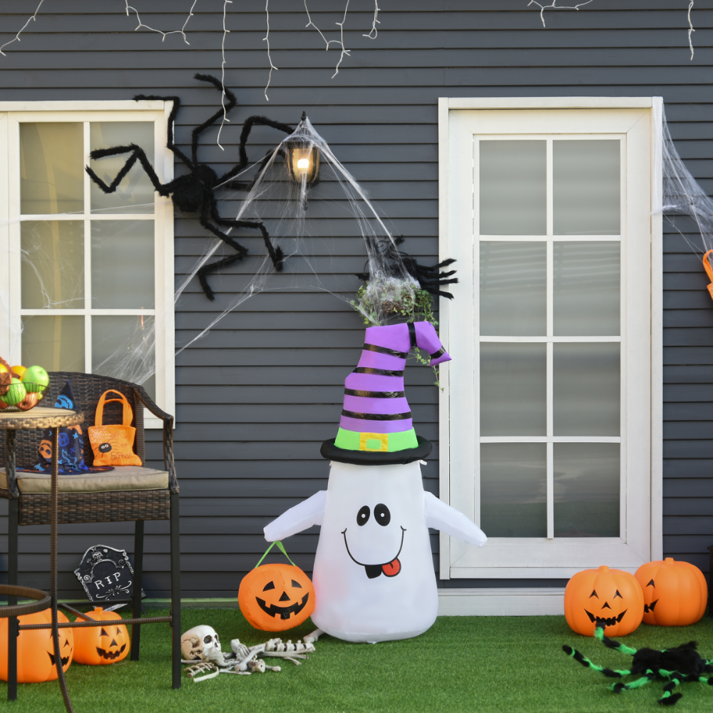 Halloween-themed outdoor decoration with ghost inflatable, pumpkins, and spider webs on a house exterior.